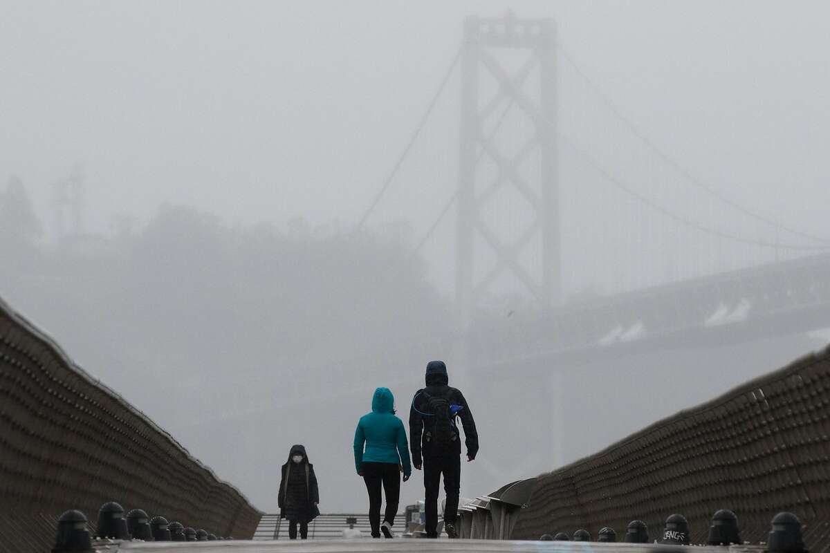People walk along Pier 14 with the Bay Bridge in the background in San Francisco, California during a steady rainfall. The first significant rainstorm of the season hit the San Francisco Bay Area on Nov. 17, 2020.