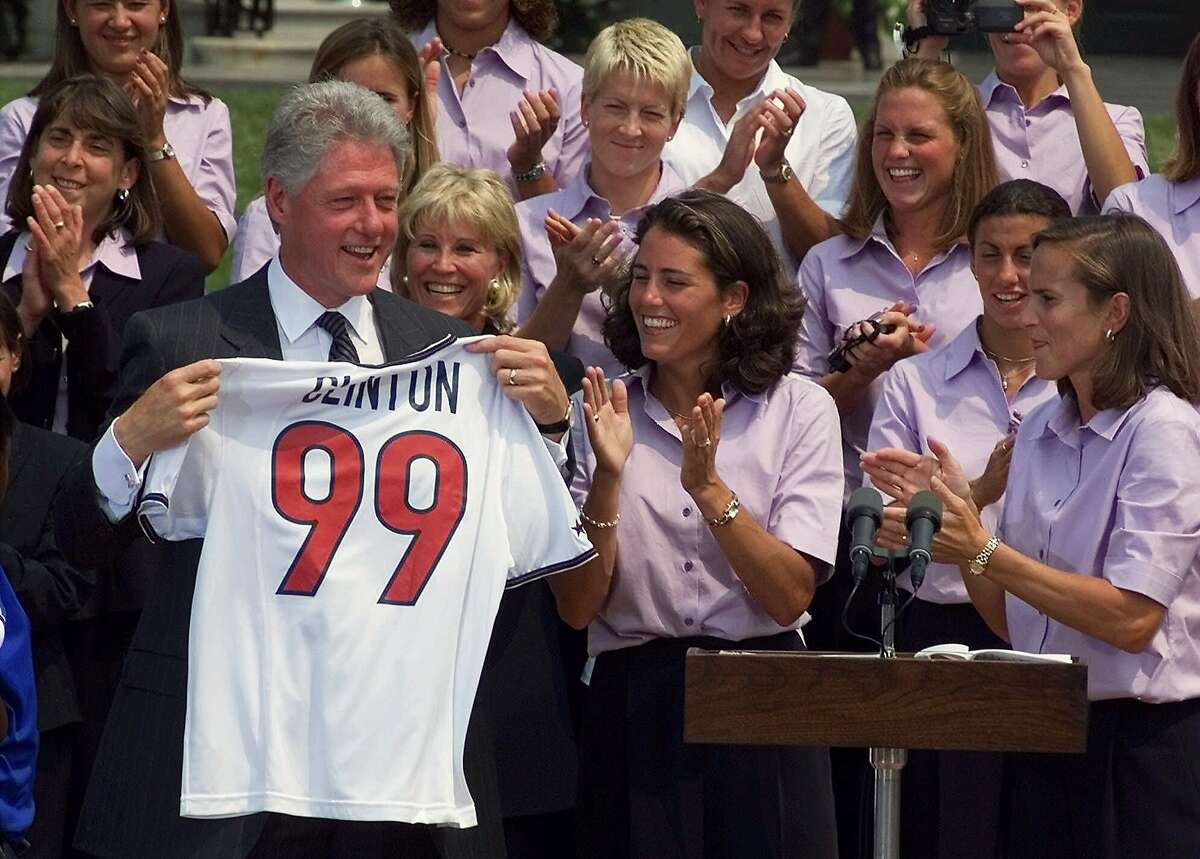 President Clinton holds up a women's U.S. World Cup Soccer jersey that was given to him by co-captain Julie Foudy, center, and Carla Overbeck, right, during a cermony on the South Lawn of the White House Monday July 19, 1999. President Clinton marked "a moment of celebration and a moment of sadness" Monday, welcoming the World Cup-winning U.S. women's soccer team to the White House and pausing to remember John F. Kennedy Jr., his wife and her sister. (AP Photo/Dennis Cook)