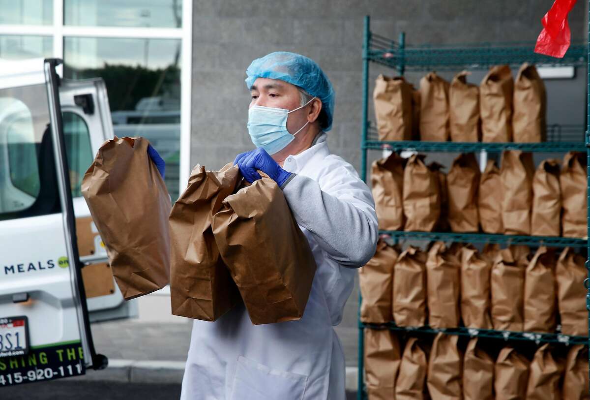 Bernard Flores carries packaged meals to delivery vans at the Meals on Wheels kitchen and distribution center in San Francisco, Calif. on Wednesday, Nov. 11, 2020. The new facility, which features a 25,000 sq. ft. kitchen and can prepare as many as 30,000 meals a day, opened in late October just in time for the busy holiday season.