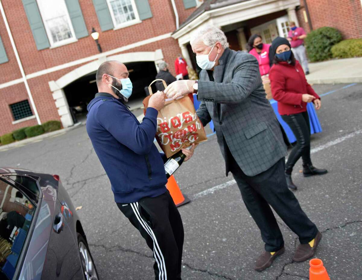 Greenwich's Antonio Silva, left, accepts a Thanksgiving meal from Boys & Girls Club of Greenwich board member Bill Farrell during the Thanksgiving meal distribution at the Boys & Girls Club in Greenwich, Conn. Tuesday, Nov. 24, 2020. Instead of the usual buffet-style dinner for club kids, this year the Boys & Girls Club handed out Thanksgiving dinners fit to feed a family of six. More than 100 club families were fed full Thanksgiving meals of a rotisserie chicken, cornbread, stuffing, mashed potatoes, pies, and sparkling wine.