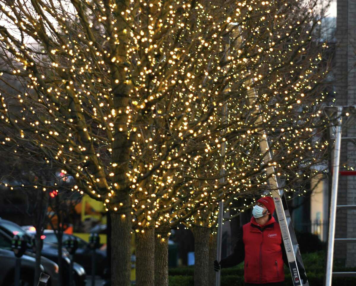 Marvin Velasquez, of Christmas Lighting Company, installs strings of lights on the trees outside Restoration Hardware in downtown Greenwich, Conn. Tuesday, Nov. 24, 2020. The private effort behind those lights is now looking to bring American flags to Greenwich Avenue.