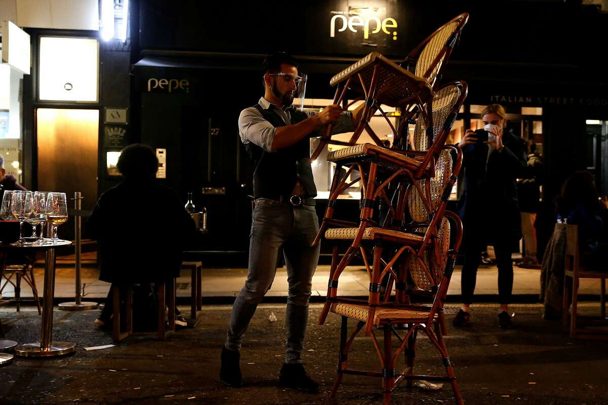 TOPSHOT - A worker stacks chairs as he packs away outdoor seating ahead of closing time outside a bar in central London on November 4, 2020, on the eve of a second novel coronavirus COVID-19 lockdown in an effort to combat soaring infections. - English pubs call last orders at the bar for a month on Wednesday evening, as the country effectively shuts down from November 5, for the second time this year to try to cut coronavirus cases. Prime Minister Boris Johnson insisted that the lockdown for England would end "automatically" in four weeks, as he tried to placate party critics over the spiralling economic fallout. (Photo by Hollie Adams / AFP) (Photo by HOLLIE ADAMS/AFP via Getty Images)