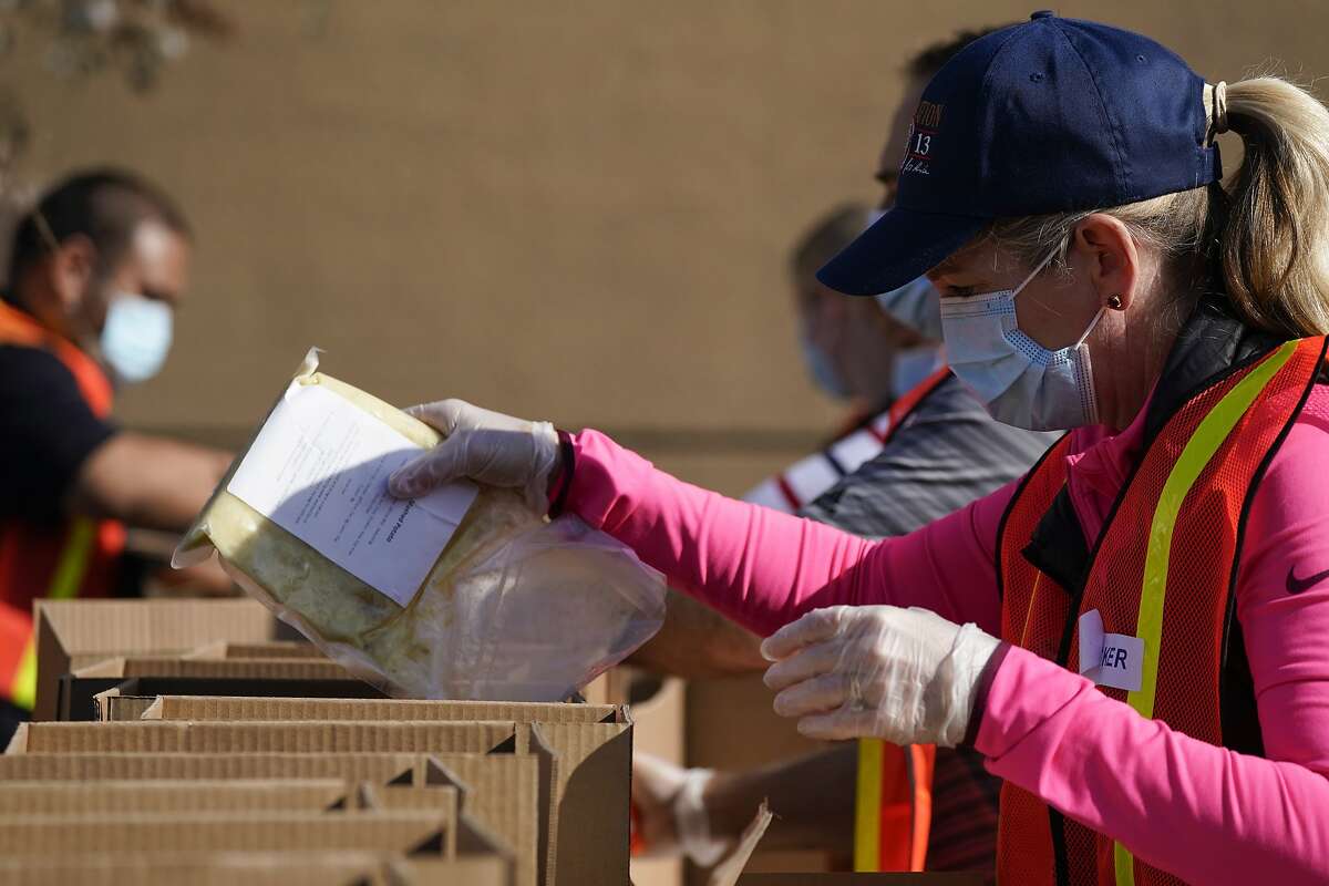 Liz McNabb, right, and other volunteers pack boxes of food outside Second Harvest Food Bank in Thursday, Nov. 19, 2020, in Irvine, Calif. The boxes will be distributed to families in need on Thanksgiving Day at the Honda Center in Anaheim, Calif. As COVID spreads and unemployment rates rise, food distribution centers see an increase in need for the holidays. (AP Photo/Ashley Landis)