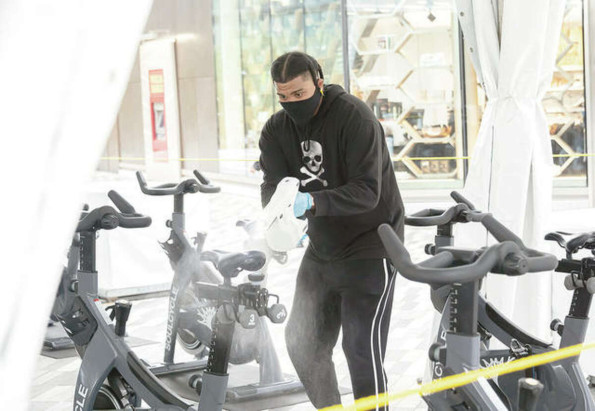 A worker sprays exercise bicycles with a disinfectant.
