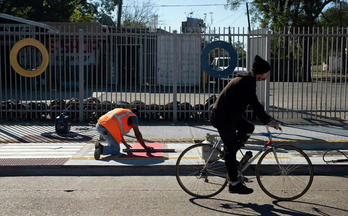A bicyclist pedals by as workers install a crosswalk on a bike lane near Cavalcade Street and the Interstate 45 frontage road on Nov. 17, 2020, in Houston. Metropolitan Transit Authority is extending the bike lane along Cavalcade Street from Irvington to Elysian as part of a $1.3 million project. This extends the existing bike lane which runs from Airline to Irvington and improves access to the Red Line light rail.