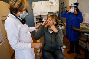 Dr. Cynthia Brattesani (left) chats with patient Kris Leifur (center) after fixing her cracked teeth and giving her a new mouthguard on Monday, Nov. 30, 2020 in San Francisco, California.