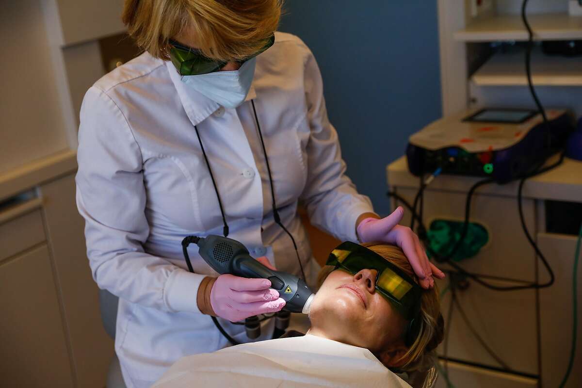 Dr. Cynthia Brattesani (left) gives patient Kris Leifur a laser treatment to loosen her jaw muscles before fixing several cracks in her teeth and giving her a new mouthguard to prevent clenching her jaw on Monday, Nov. 30, 2020 in San Francisco, California.