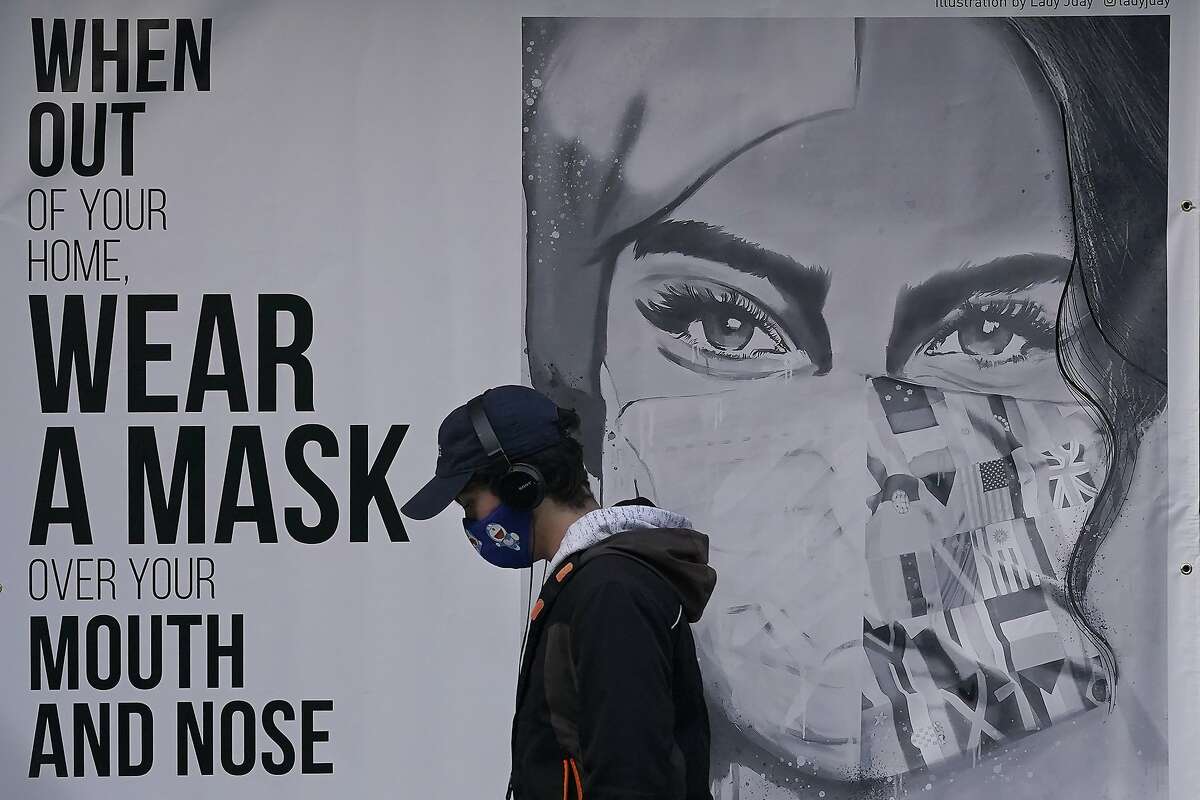 FILE - In this Saturday, Nov. 21, 2020, file photo, a pedestrian walks past a mural reading: "When out of your home, Wear a mask over your mouth and nose," during the coronavirus outbreak in San Francisco. San Francisco is joining a statewide curfew and Silicon Valley is banning all high school, collegiate and professional sports and imposing a quarantine for those traveling into the region from more than 150 miles away. Santa Clara County has the highest case rate in the Bay Area, leading to the stricter rules, said Santa Clara County Health Officer Dr. Sara Cody. (AP Photo/Jeff Chiu, File)