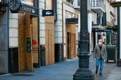 A man passes stores that are boarded-up but open under San Francisco virus regulations.