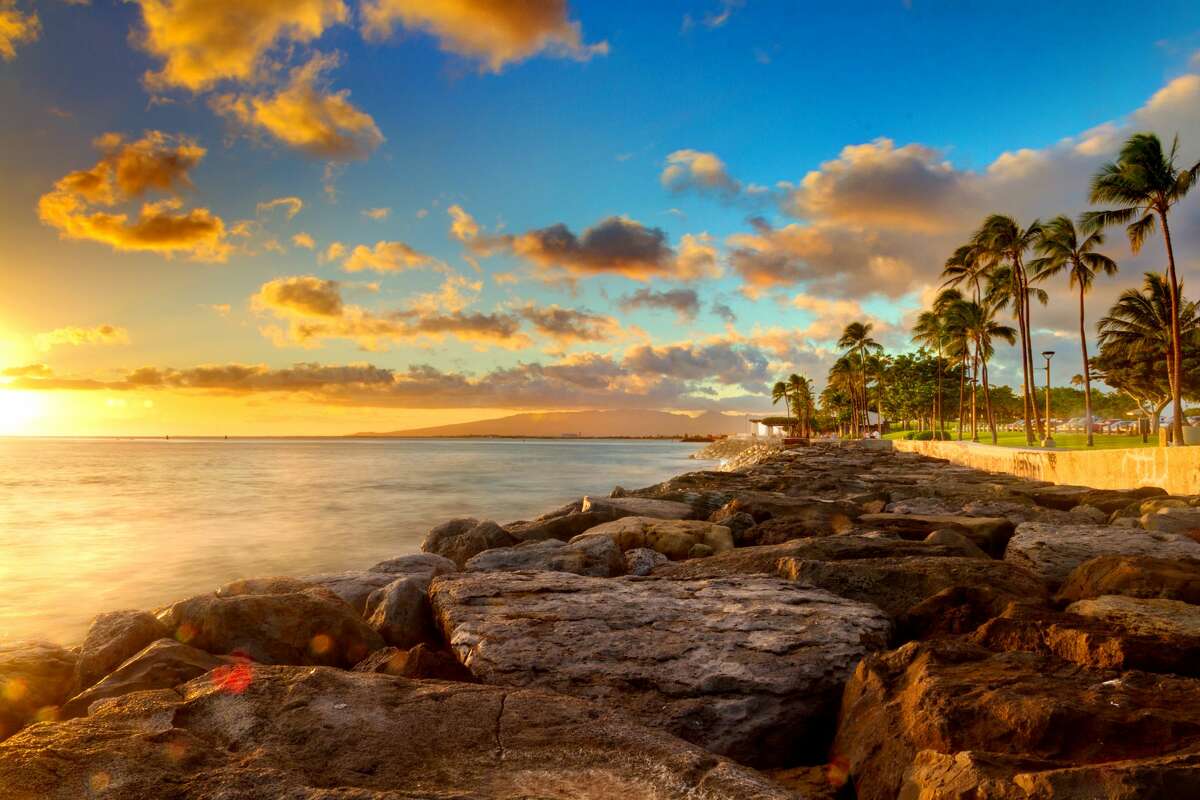 This could be your office: An ocean sunset over rocks and palm trees at beachfront park Kaka'ako on O'ahu, Hawaii.