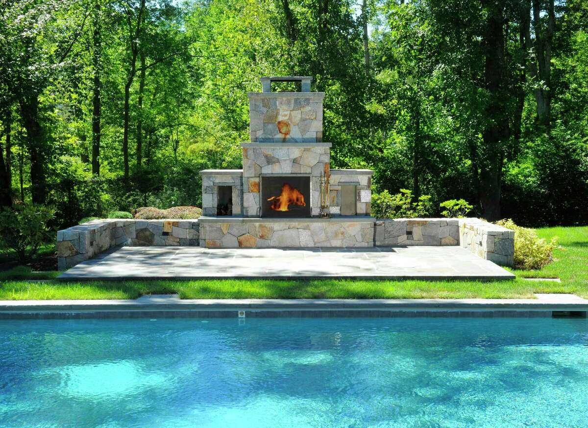 The outdoor fireplace at 12 Carrington Drive, Greenwich, sits poolside and among 4.01 acres. Houlihan Lawrence is the listing brokerage for the property; the current asking price is $2.495 million.
