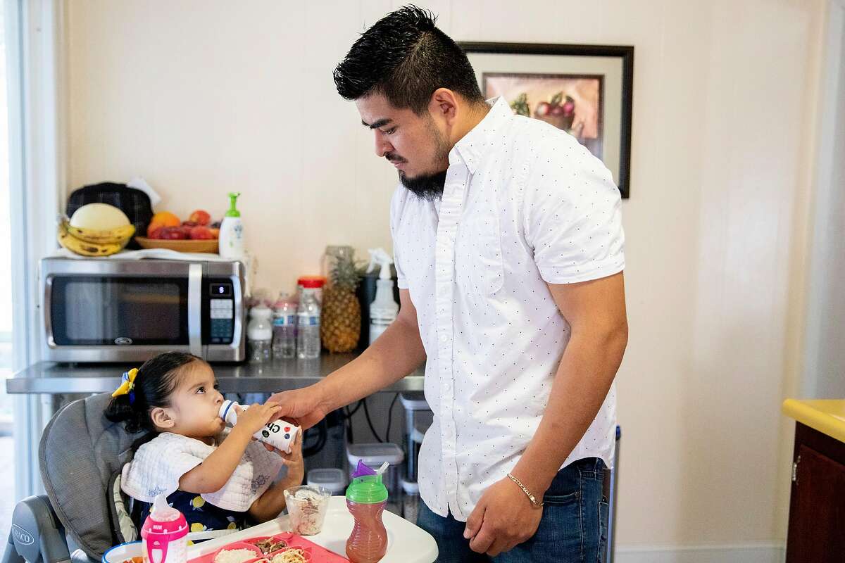 Gamalia Castillo-Becerril helps his daughter Lily, 1, drink milk during breakfast time at their home in Napa, Calif. Saturday, November 28, 2020. Rosa Alvizar Gutierrez and her husband Gamalia Castillo-Becerril both had their jobs cut back or furloughed in March. Chronicle Season of Sharing paid their rent for April and money owed for utilities. They are both back at work now.