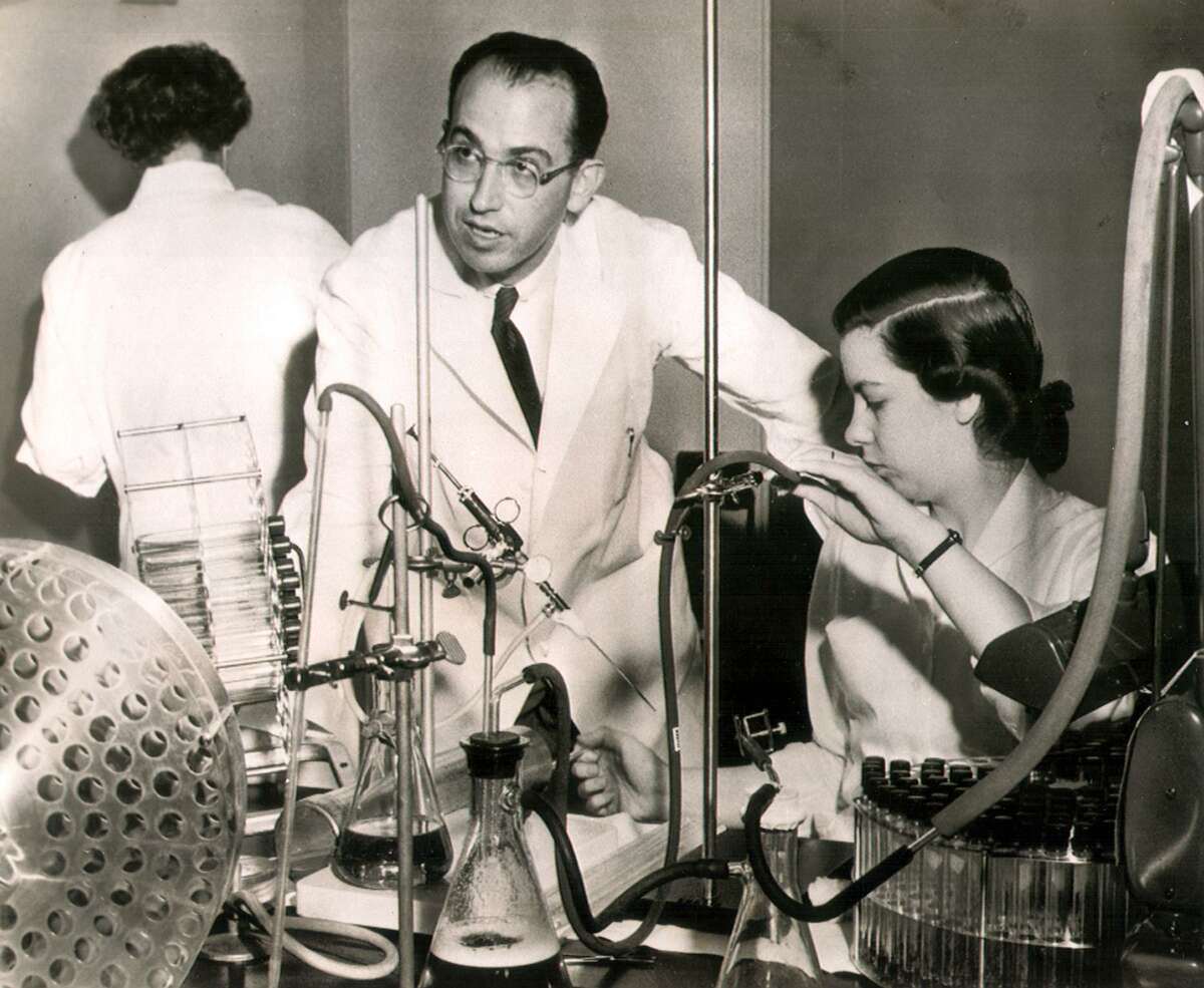 1954: Dr. Jonas E. Salk, a University of Pittsburgh bacteriologist whose polio vaccine will get a nation-wide test next month, supervises a laboratory process on the vaccine. Mrs.Ethel Bailey. research assistant in bacteriology, draws fluid from culture tubes. In the upcoming field tests, between 500,00 and a million children will get trial shots of the vaccine. At summer's end it can be learned whether the vaccine will end the dreaded polio.
