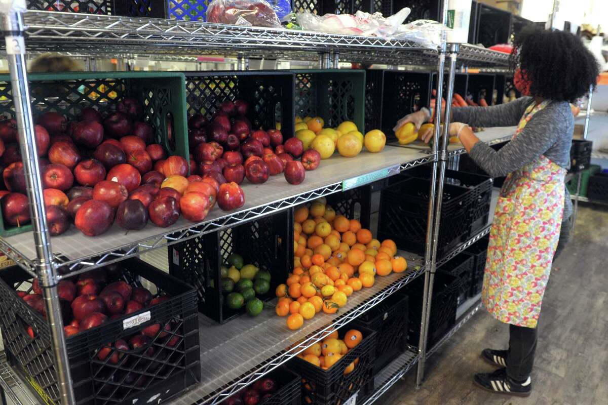 Volunteer Christina Randall stocks shelves with donated fresh fruit and vegetable at the Person-to-Person food pantry in Norwalk, Conn. Nov. 17, 2020.