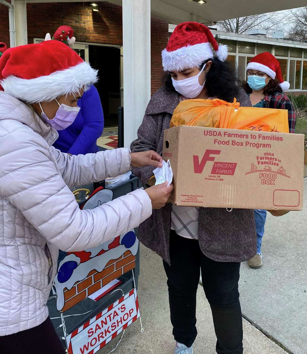 Marie DeOliveira, a New Milford social worker and diverse community advocate with the department, left, and volunteer Layla Faridani, verify the tag on the box before handing it to a family during the Santa Fund gift distribution on Dec. 4, 2020.