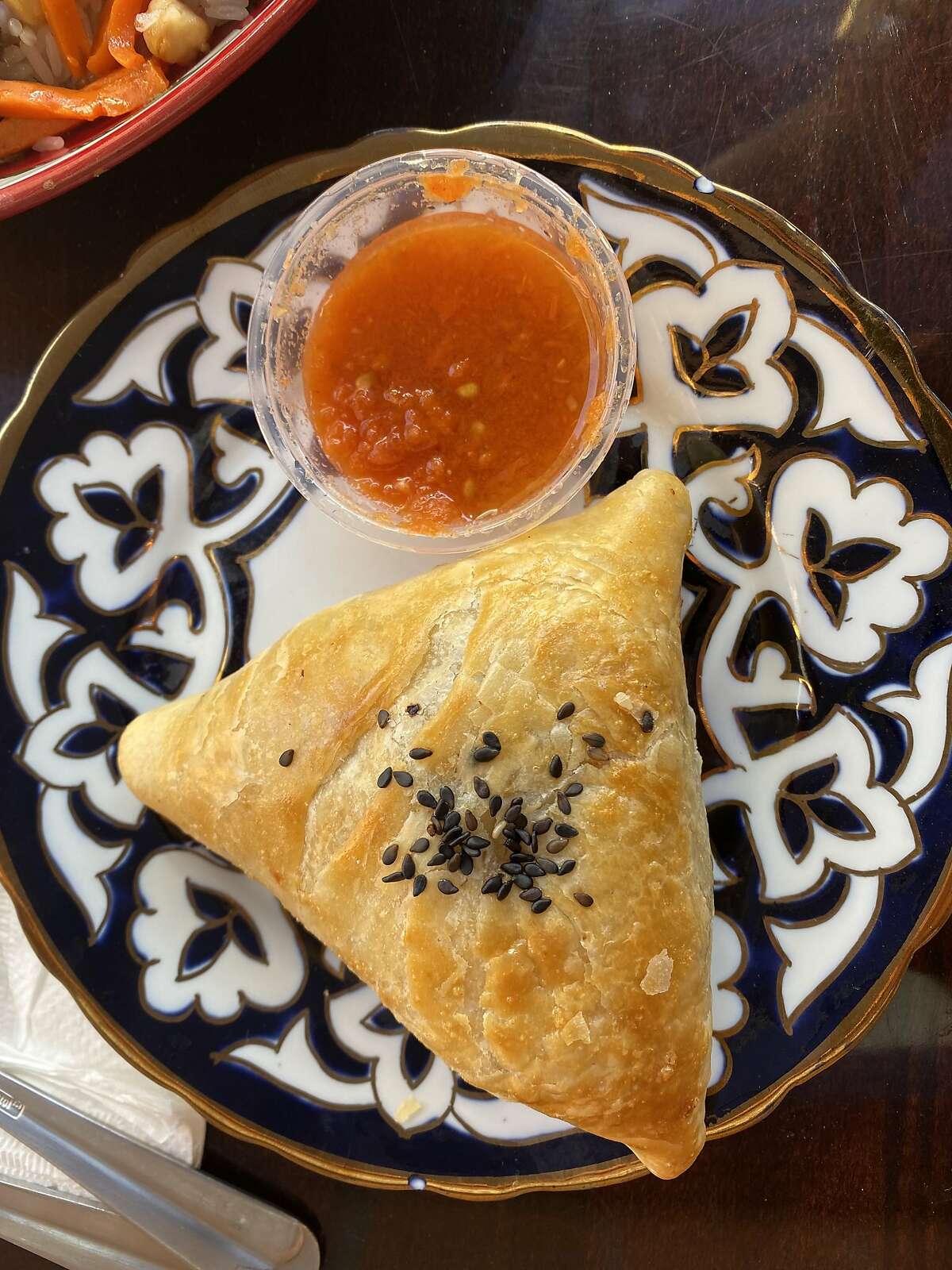 The hearty baked samsa of Halal Dastarkhan in S.F. is accompanied by a mild tomato-based sauce.