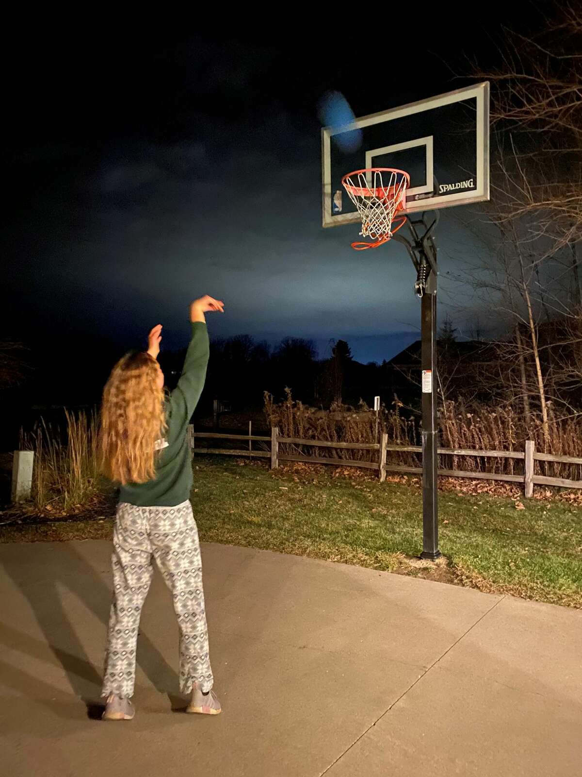 Freeland team co-captain Hannah Niederquell shoots baskets in her driveway late at night as part of a challenge held in honor of former Falcons' coach, the late Tom Zolinski, to commemorate the one-year anniversary of his passing.