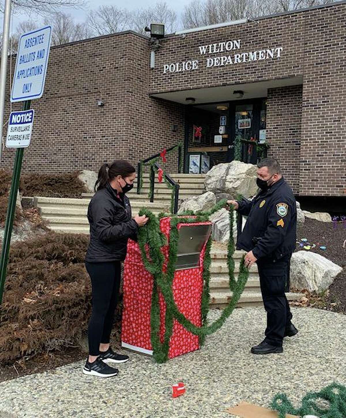 Wilton Social Services Director Sarah Heath and Sgt. Anthony Cocco of the Wilton Police Department, decorate the ballot box, ready for its new role as Santa’s Mailbox.