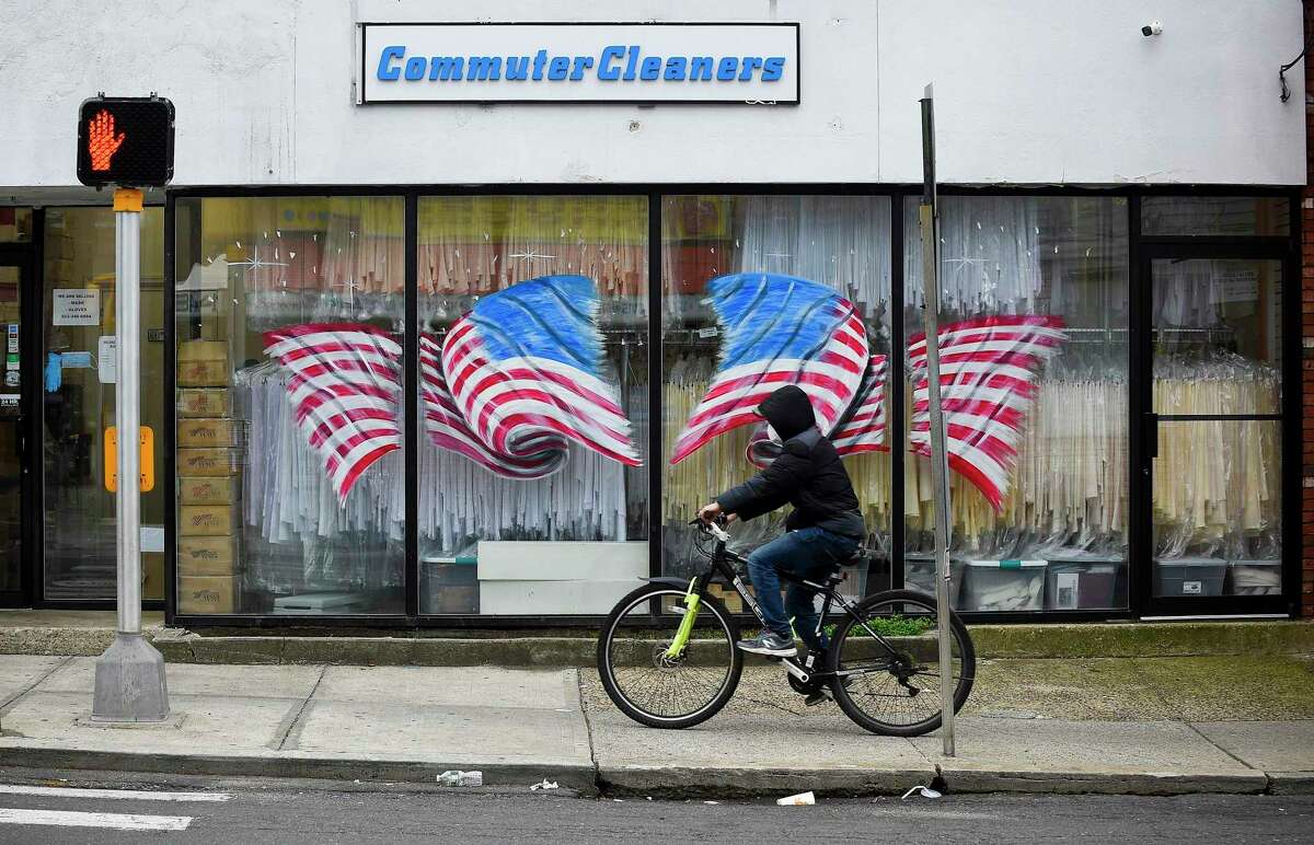 A bicyclist passes in front of American Flags displayed on the windows of Stamford Uniform in Stamford, Connecticut on April 29, 2020. Owner Paul McDonald has seen a dramatic decrease in business as a direct result of the COVID-19 pandemic.