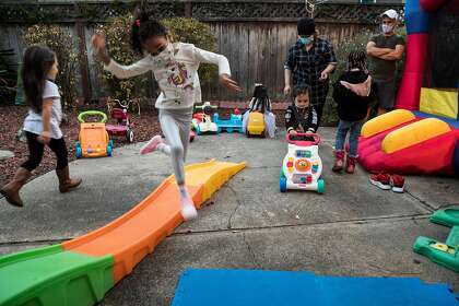 Lilliana Vallete, 5, leaps over a slide while all the kids play under the supervision of Fouziya Bawazir and her son, Abadi Bawazir at Wishing Well Daycare in Hayward, Calif., on Wednesday, December 9, 2020. Fouziya Bawazir runs a 24-hour day care center in her home in Hayward. She takes care of 15 kids, from five families. 10 are there during the day and five come overnight while their single parents work graveyard.