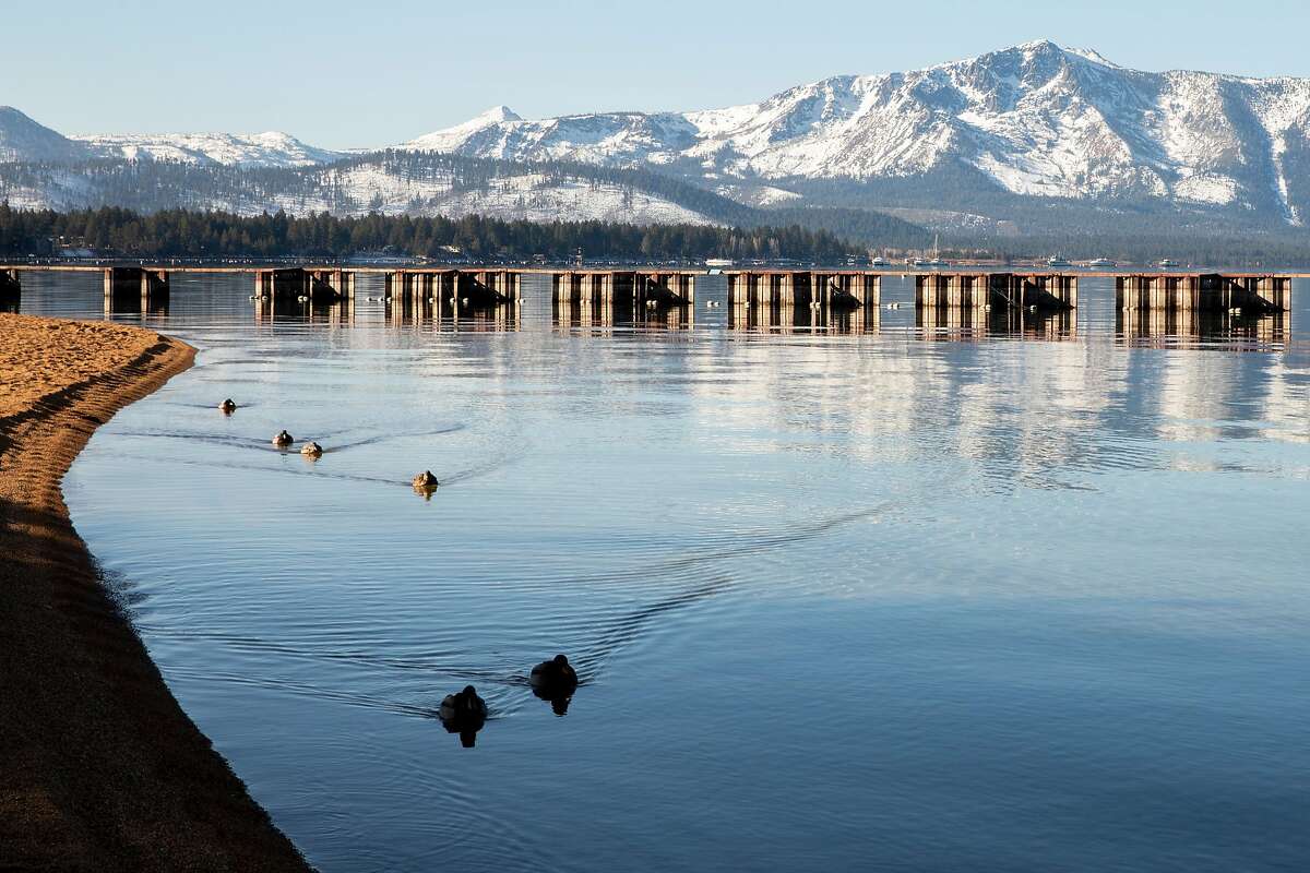 Ducks glide across glassy waters as mountains dusted in snow are seen in South Lake Tahoe on Dec. 10 as the region was about to fall under a ban on vacation travel due to a rise in the number of COVID-19 hospitalizations.