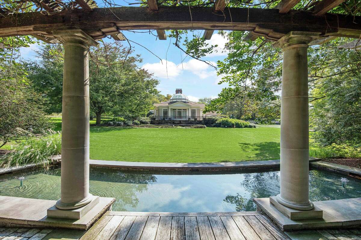 Reflecting pool and arbor at 1211 Old Academy Road, Fairfield. A pergola-like arbor, reflecting pool, and beautiful lit fountain offer an enchanting place to relax in the shade, looking back toward the main house, the agent said. One of the most unusual and beautiful spaces is the English conservatory, which features a multi-vault, wood-paneled ceiling with a glass dome, under which are found tall windows topped with colorful stained glass transoms, a built-in bar and distinctive in-laid wood flooring. The family room has a vaulted ceiling with exposed beams and a wet bar.