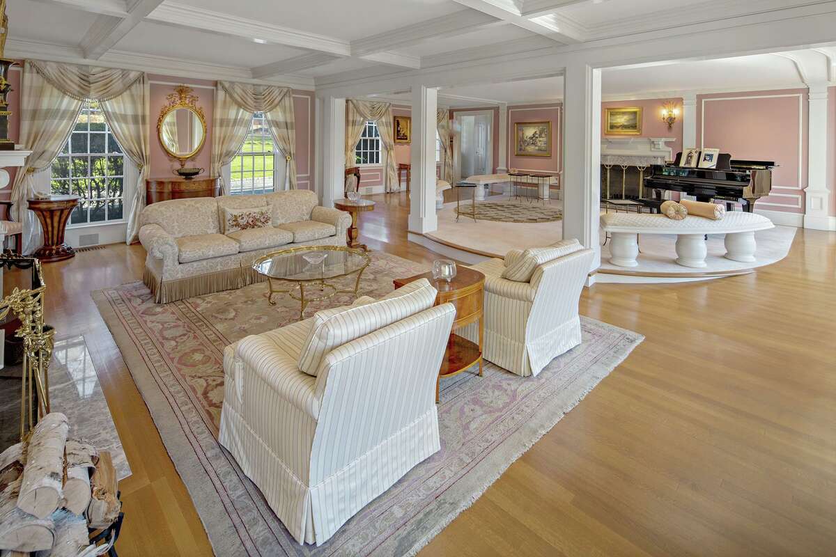 Living room with two fireplaces at 1211 Old Academy Road, Fairfield. In the formal living room there are two marble fireplaces, one at both ends, and a raised circular platform for placement of a grand piano to match the grand setting. The wood-paneled home office has a fireplace of its own, as does the second floor master bedroom suite. A large en suite bedroom offers an opportunity for a first floor master or in-law suite. One of the other bedrooms currently serves as another home office, providing ample space for long distance working or schooling.