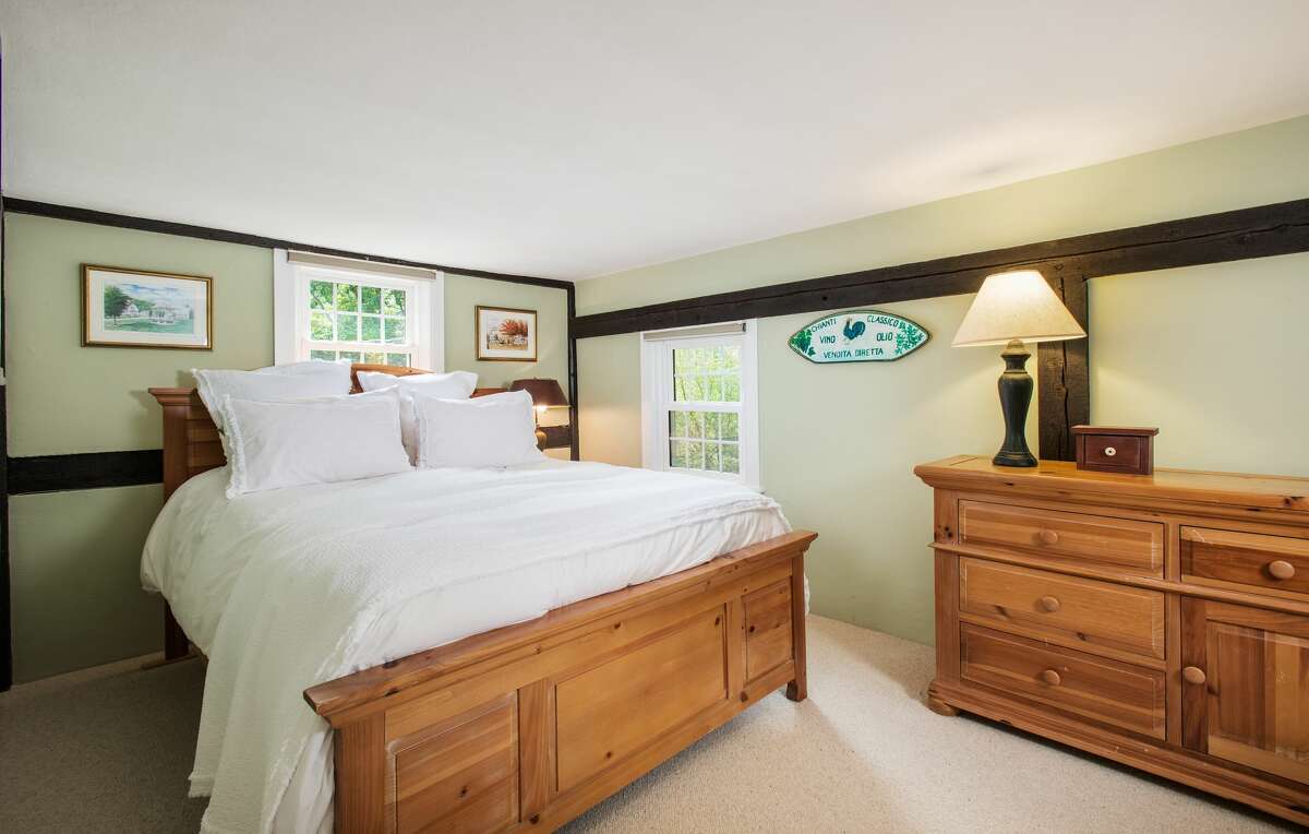 Master bedroom at 28 Valley Road, Westport. The kitchen is open to a dining area with two bay windows, both with built-in window seats that look over the half-acre property. There is also a wall of built-in storage cabinets for culinary ware. In the master bedroom, features include original exposed timbers, wood flooring covered in new wall-to-wall carpeting, and a walk-in closet. The second bedroom offers a built-in, floor-to-ceiling display or book shelving and lots of natural light, while the third bedroom has a built-in bed with storage drawers, and authentic wood paneling on the walls, the agent said. This room can also be used as an office.