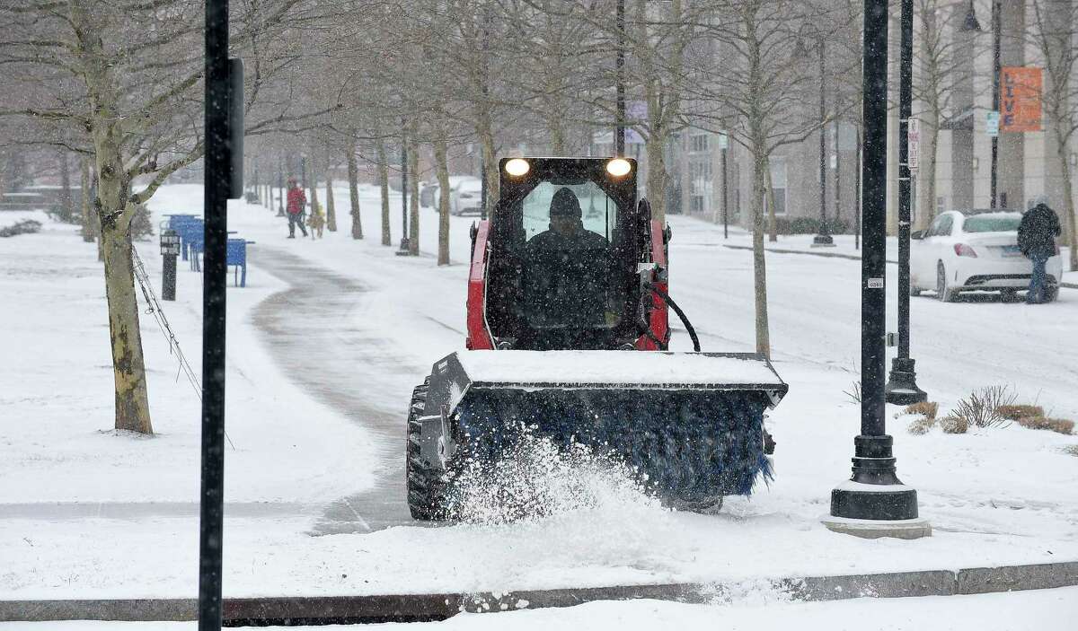 A worker clears snow from the walkways surrounding Harbor Points Common Park last February. With heavy snowfall predicted for Wednesday, Mayor David Martin declared a snow emergency.