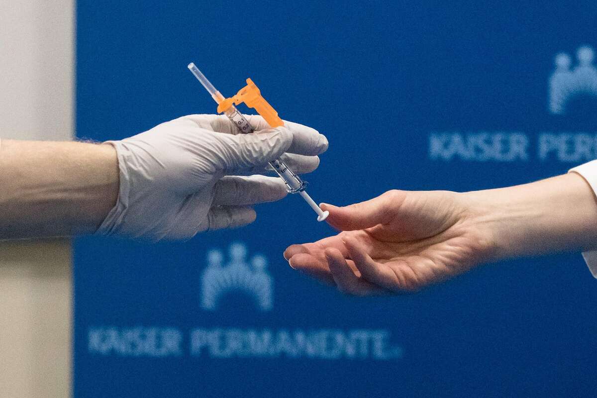 Kaiser Nurse Scott Keech (left) receives a needle from another employee to administer one of the first ten Pfizer COVID-19 coronavirus vaccines to frontline workers at Kaiser San Francisco hospital on December 17, 2020.
