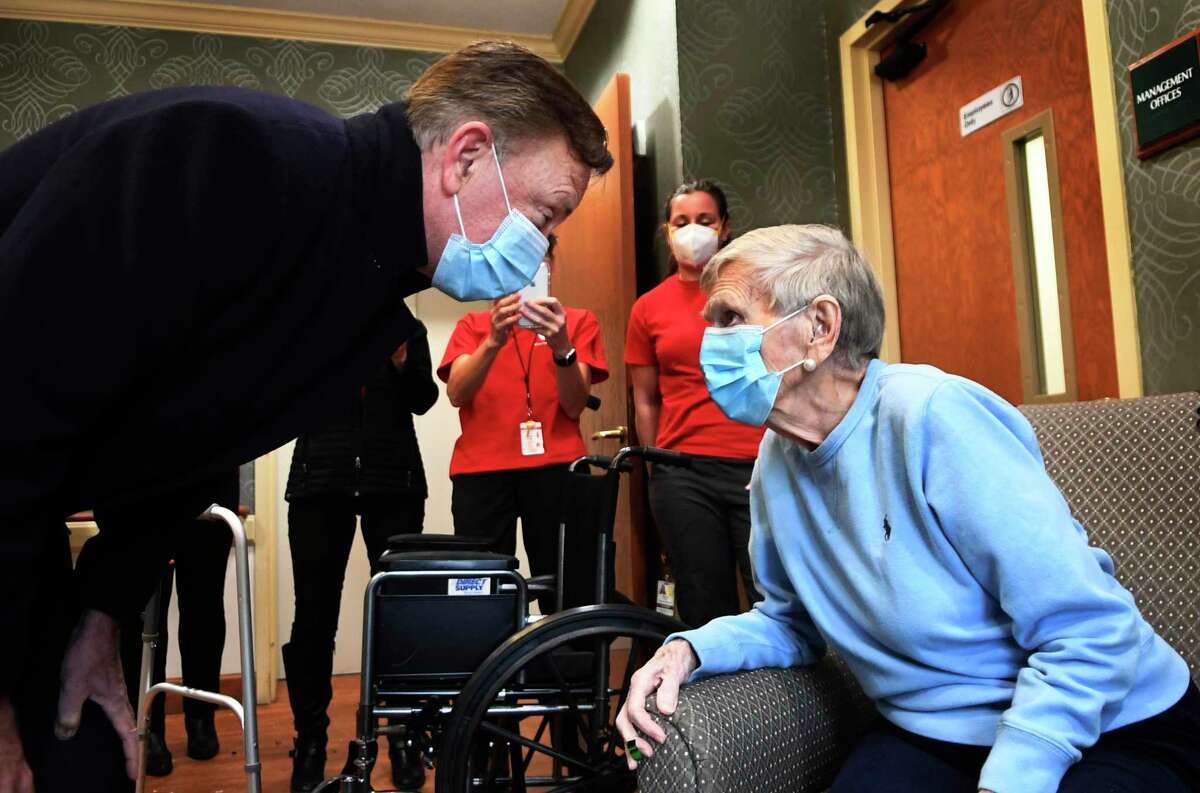Gov. Ned Lamont greets Jeanne Peters, 95, a rehab patient at The Reservoir, a nursing facility in West Hartford, after she was given the first COVID-19 vaccination at the nursing home Friday, Dec. 18, 2020. The home, owned by Genesis HealthCare, is among those where a strike has been authorized.