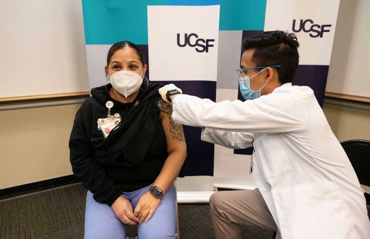 Reina Lopez, left, a patient support assistant in UCSF reception services, receives a COVID-19 vaccine from Matthew Aludino, a fourth-year student at the School of Pharmacy, among the first recipients to receive inoculation, in a medical sciences clinic building on the Parnassus Heights campus.