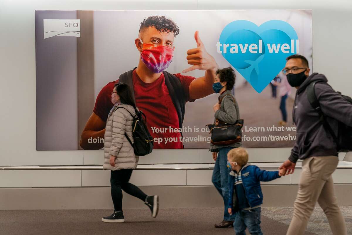 A family walks past a sign urging safe travel during the pandemic at San Francisco International Airport, December 18, 2020.