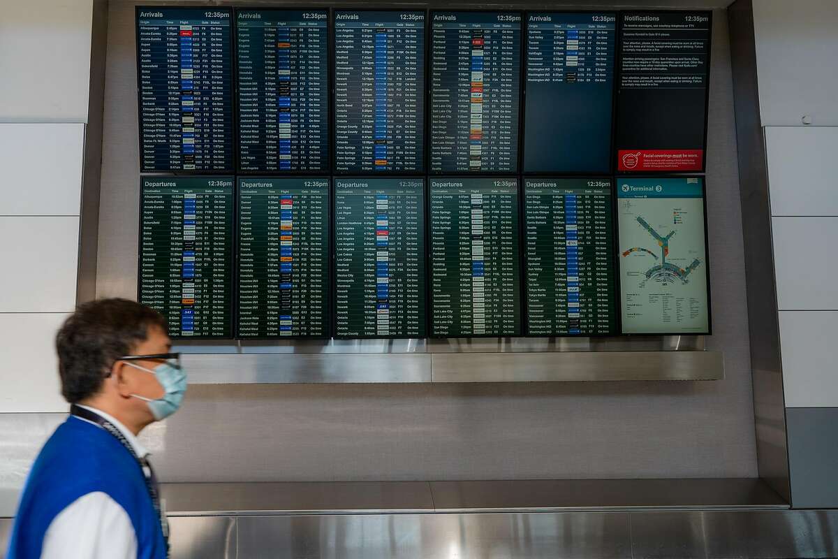 An airport employee walks past arrival and departure screens at San Francisco International Airport on Friday, December 18, 2020.
