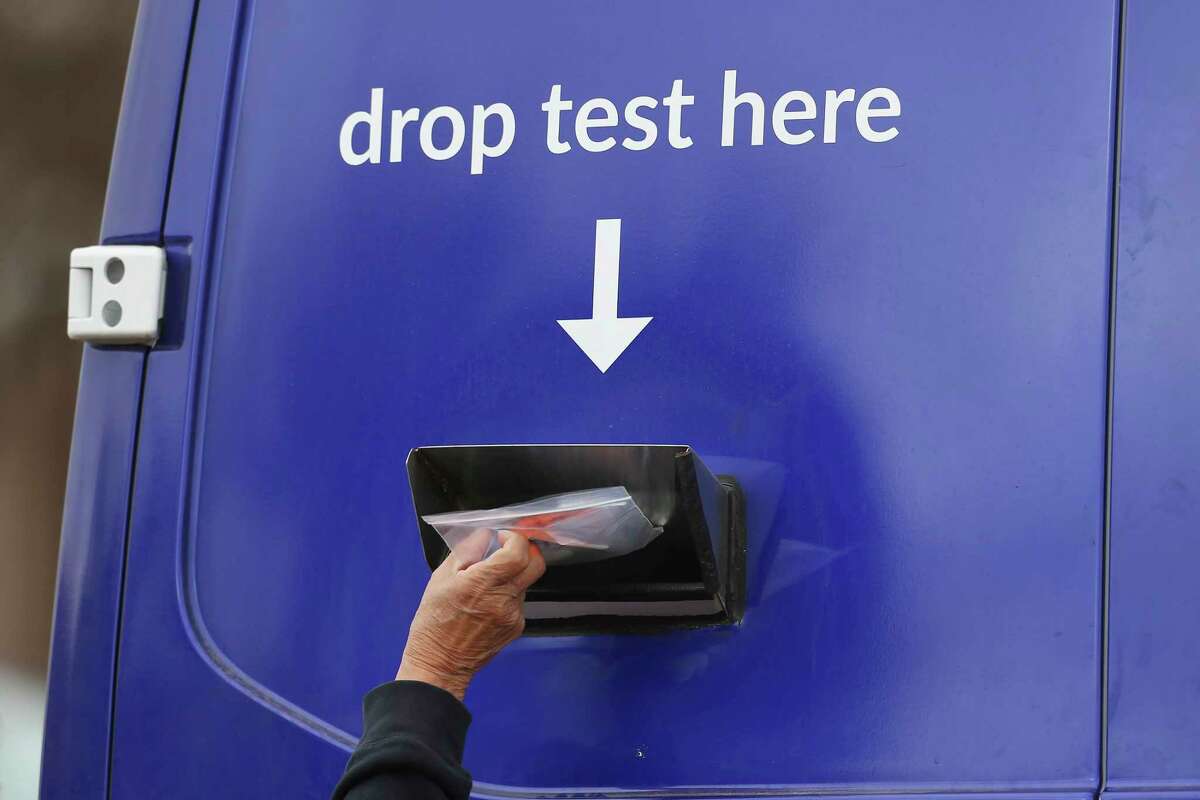 A person drops a test bag into a slot at a COVID-19 popup testing site on South Zarzamora Street on Friday.