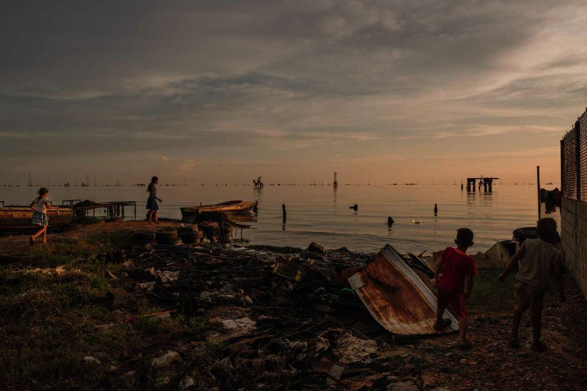 Children playing on abandoned fishing docks soaked in crude oil in Cabimas, Venezuela, Sept. 19, 2020. Refineries that once processed oil for export are rusting hulks, leaking crude that blackens shorelines and coats the water in an oily sheen. (Adriana Loureiro Fernandez/The New York Times