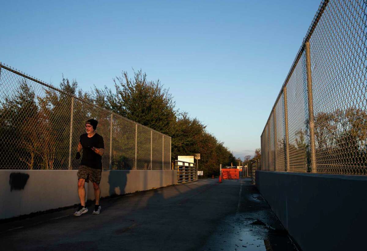 A jogger crosses a bridge on M-K-T Trail after making a turn from the White Oak Bayou Trail Wednesday, Dec. 16, 2020, at in Houston. The M-K-T Bridge, which is behind the orange barrier, carries the Heights Hike and Bike Trail across the White Oak Bayou, but it has been closed since August due to a fire.
