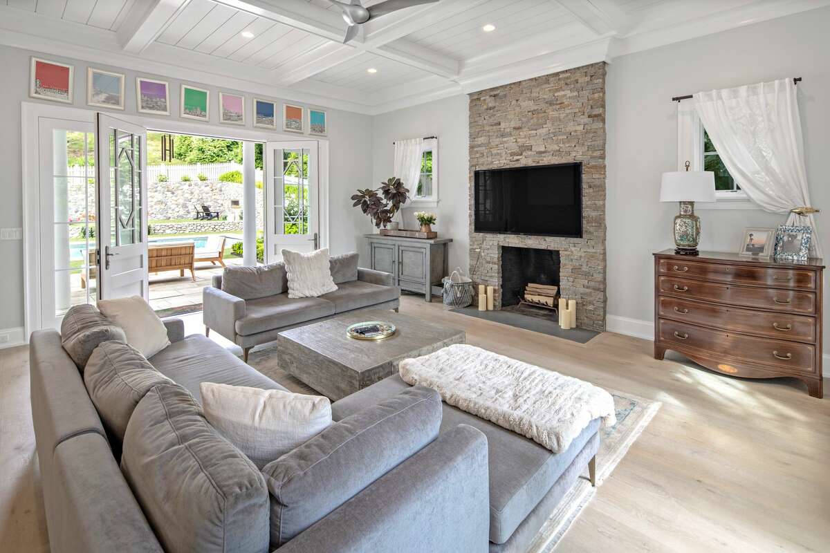 Family room with stacked stone fireplace at 2 Hidden Hill Road, Westport. The house was built in 2014, creating 9,250 square feet of living space on four finished levels. The architectural design includes a thoughtful custom, open floor plan with an abundance of windows and doors to allow natural light to shine in. The design and siting of the house take full advantage of the property's attractive setting. The