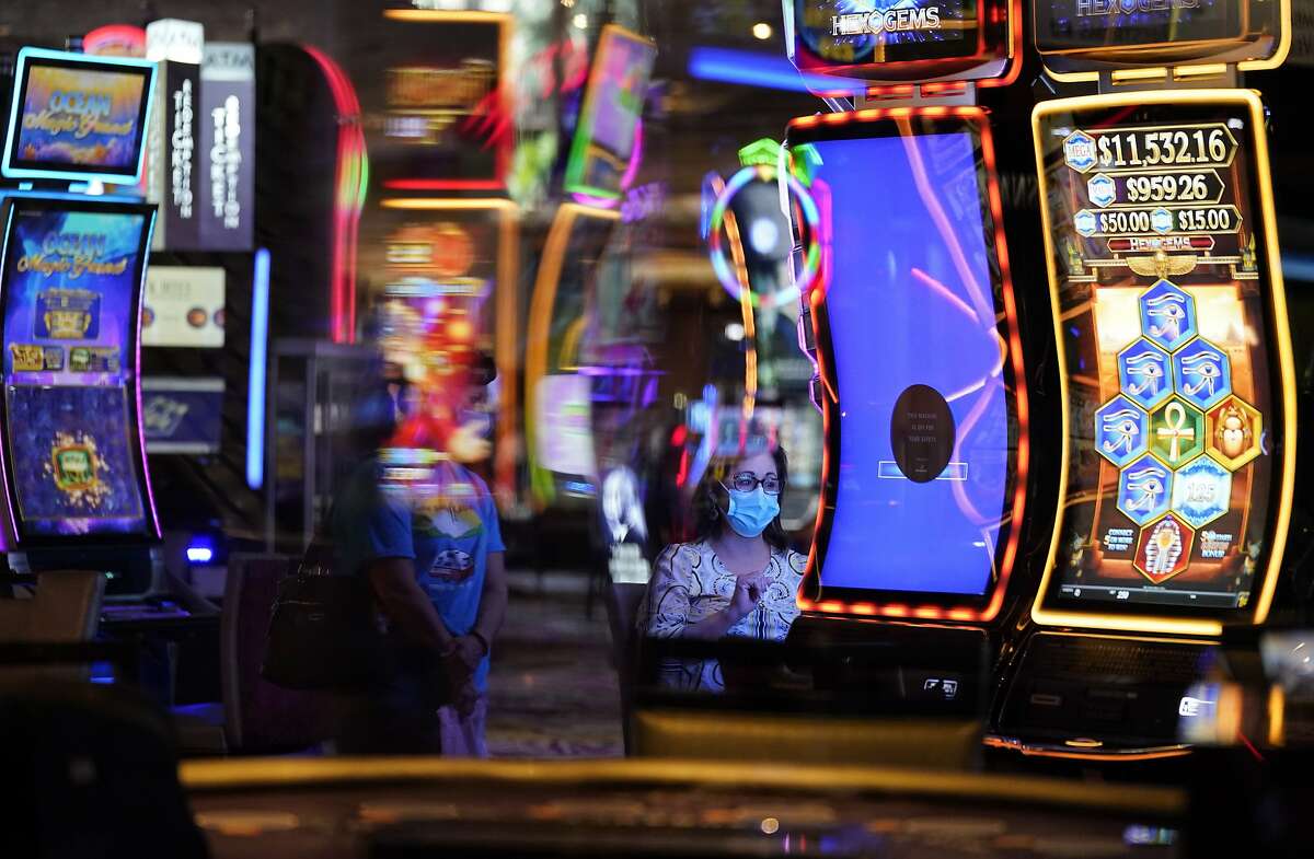 In this Aug. 27, 2020, file photo, a woman, wearing masks as a precaution against the coronavirus, plays an electronic slot machine at the Mirage hotel and casino in Las Vegas.