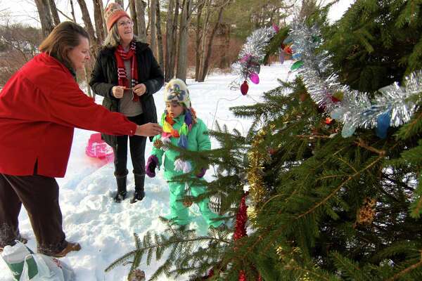 Allison Menendez hands an ornament to Maggie Young, 5, and she and members of the Shelton Land Conservation Trust gather to decorate a "Christmas Tree" that is located next to the Rec Path on the trust's Lane Street Property in Shelton, Conn., on Saturday Dec. 19, 2020. In back is Maggie's grandmother Mary King. The ornaments mainly consisted to edible ones to feed the wild birds and small animals on the property.