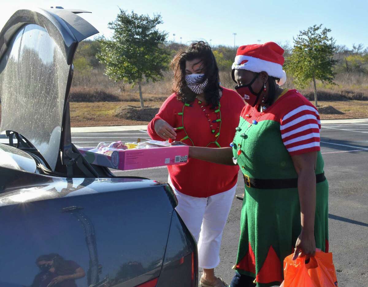 San Antonio City Councilwomen Rebecca Viagran (left) and Jada Andrews-Sullivan are dressed for the holidays as they load up the back of a vehicle with gift bags full of books, toys and more on Saturday during a holiday drive-thru giveaway.