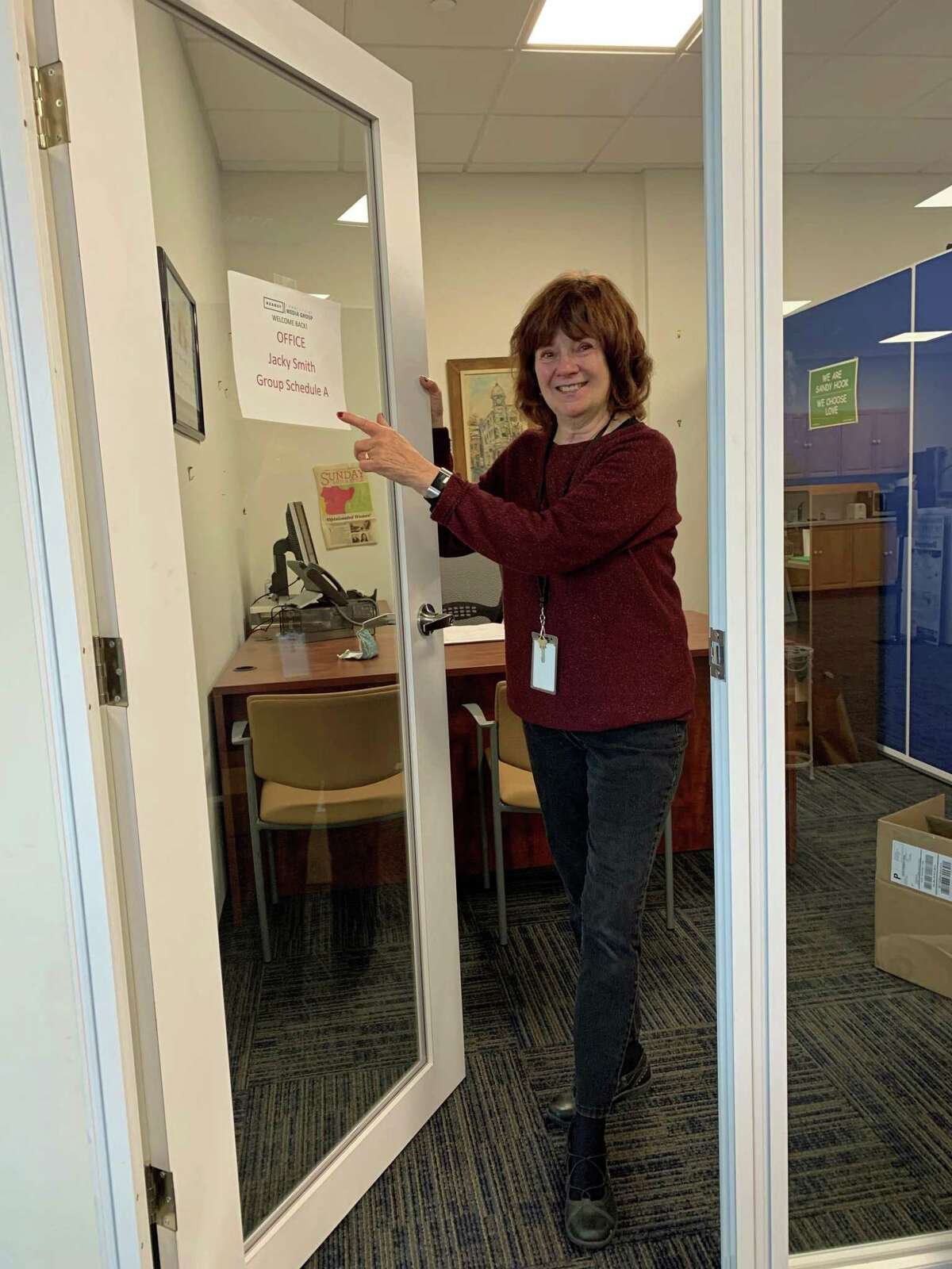 Columnist Jacqueline Smith points to the “welcome back” sign on her office door at The News-Times in Danbury. It was her first visit back since leaving in mid-March to work from home because of the pandemic. The newsroom, like many other businesses, will remain closed for the foreseeable future.