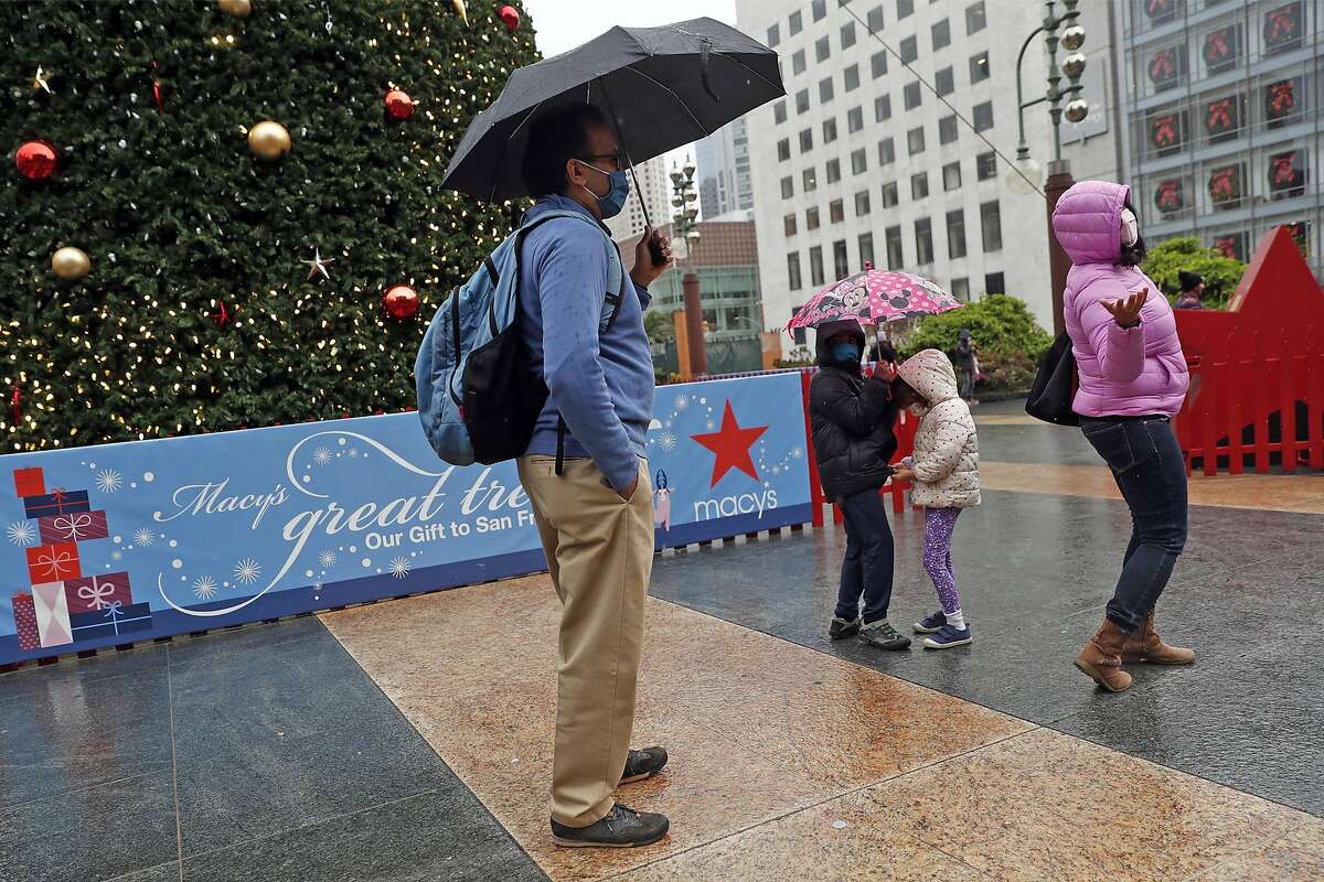 Reena Arya checks the rain, as her husband, Ambar, and children Sameer, 7, and Nuria, 4, stand under umbrellas at the Holiday tree in Union Square in San Francisco, Calif., on Friday, December 25, 2020.