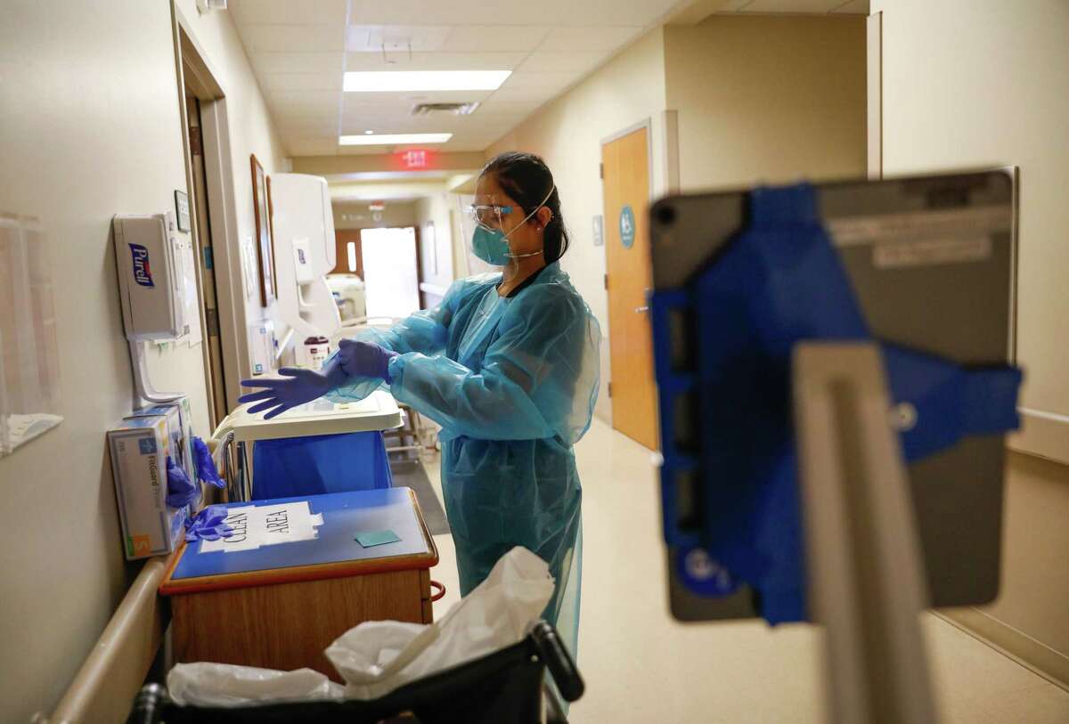 Nurse Janessa Deleon puts on gloves before bringing a tablet into the hospital room of a COVID-19 patient so the patient could video-chat with family at Regional Medical Center of San Jose early this month.