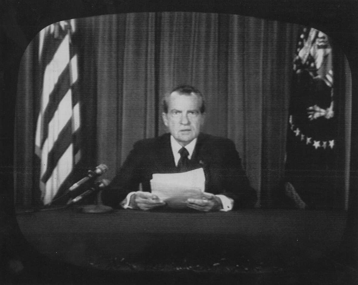 President Richard Nixon sits in the White House Oval Room flanked by the American and presidential flags as he announces in August 1974 that he will resign.