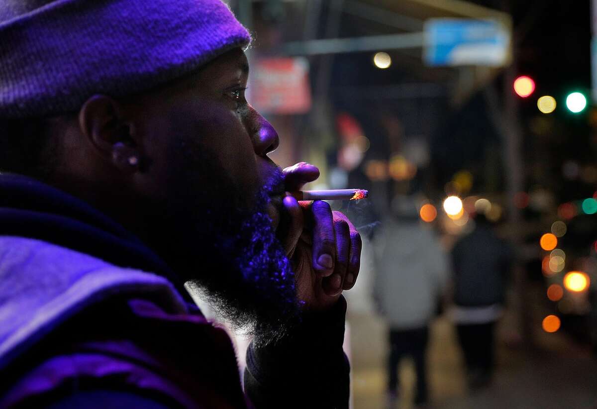 Customer Malcolm Thompson smokes one of the Newports he purchased from employee Saqr Abdulla at Evergreen Smoke Shop in Oakland, Calif., on Tuesday, December 29, 2020. One new llaw that would have taken effect on January 1, is a ban on flavored tobacco products, but it's on hold pending a possible ballot measure.