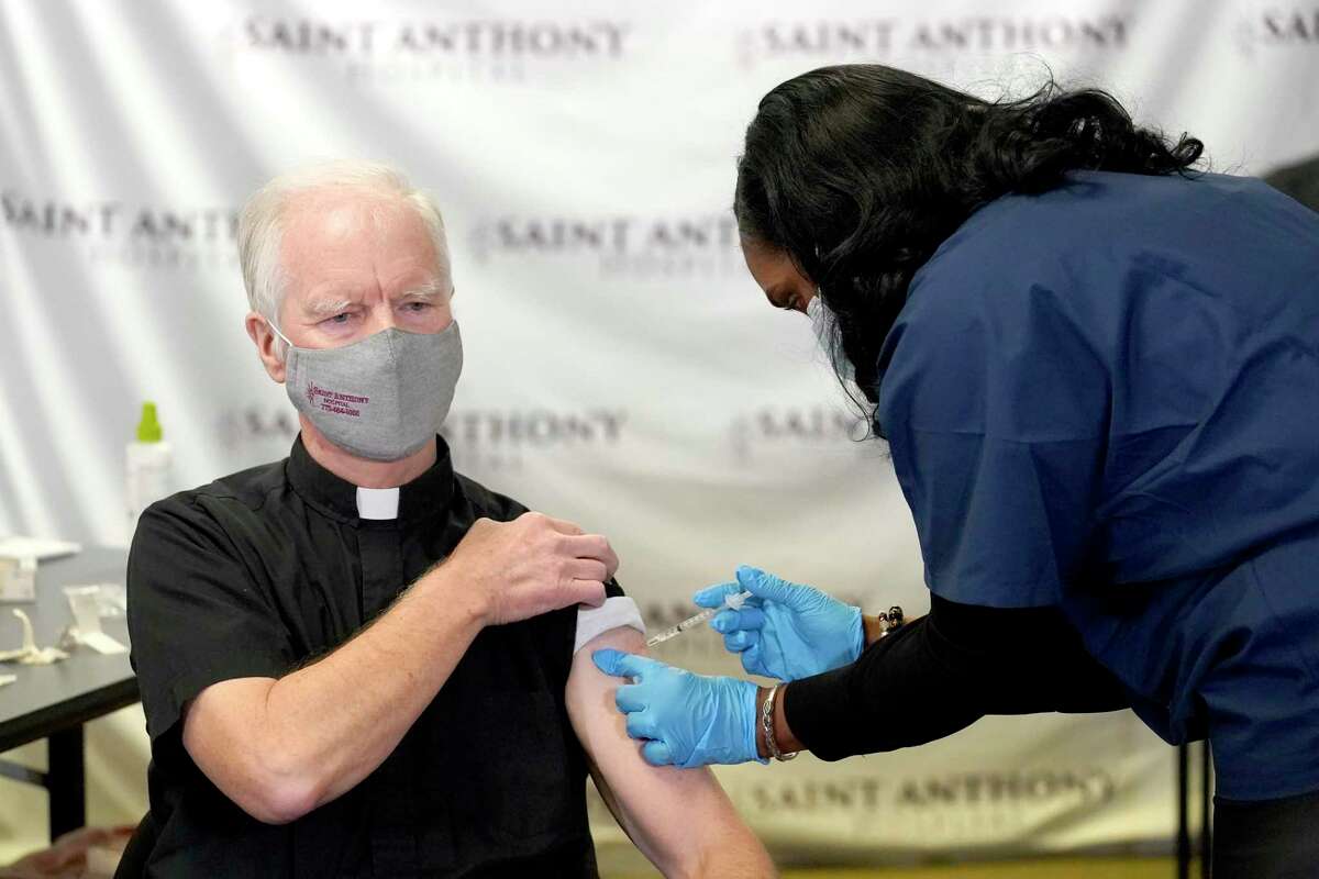 Rev. Donald Nevins, pastor of St. Agnes of Bohemia Church in Chicago, left, receives the first of the two Pfizer-BioNTech COVID-19 vaccinations Wednesday, Dec. 23, 2020, from Sherrie Spencer, Vice President Chief Nursing Officer at Saint Anthony Hospital in Chicago.