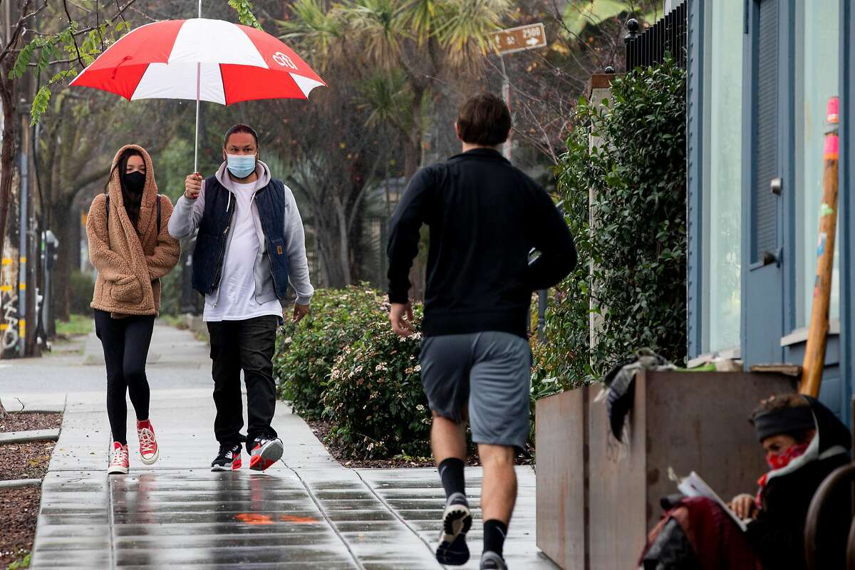 Ferdinand and Amelia Yambao of San Leandro were masks and share an umbrella while walking down Dwight Way near Telegraph Avenue as rain falls over Berkeley, Calif. Saturday, January 2, 2021. Much-needed rain is expected to fall through most of Friday in the Bay Area.