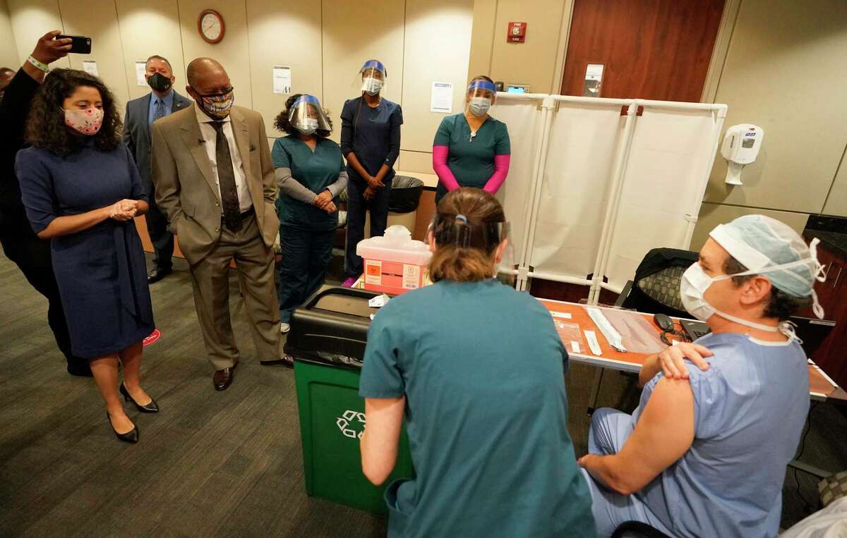 Harris County Judge Lina Hidalgo, left, Houston Mayor Sylvester Turner and others watch as Houston Methodist Hospital RN Kristin Adolphs prepares to give Nestor Esnaola, surgical director of cancer center, his COVID-19 vaccination at Houston Methodist Hospital Tuesday, Dec. 15, 2020 in Houston.