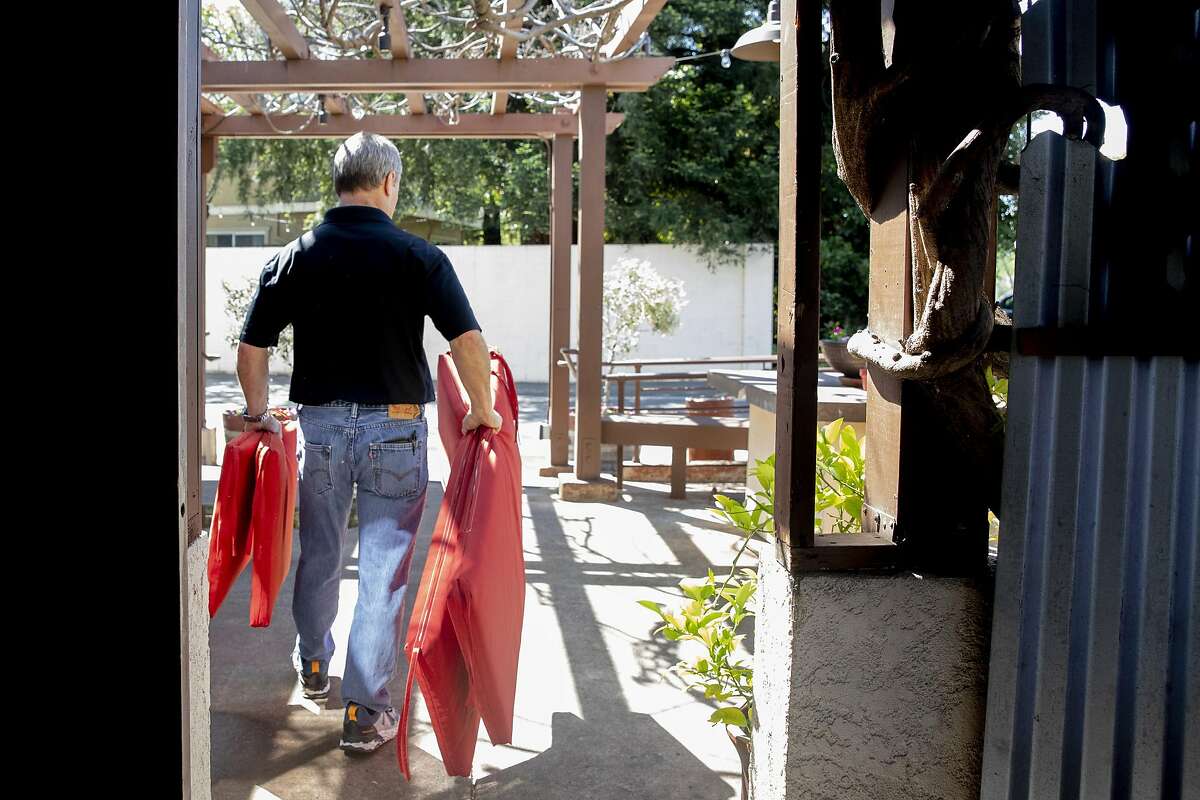 Fume Bistro owner Terry Letson carries cushions to place on outdoor seating for customers at his restaurant in Napa on May 5, 2020 in defiance of shelter-in-place orders. In December, the restaurant once again seated diners despite the shutdown.